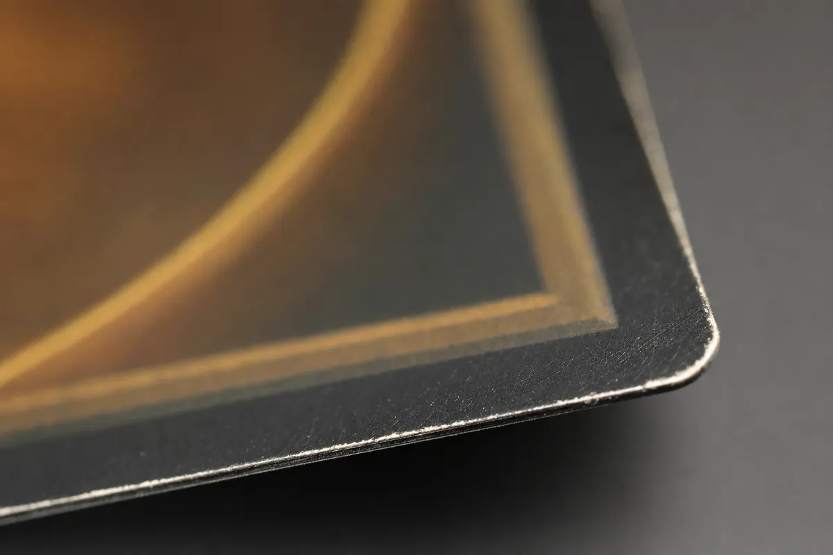 Close-up of trading card edge whitening and a soft corner under raking light
